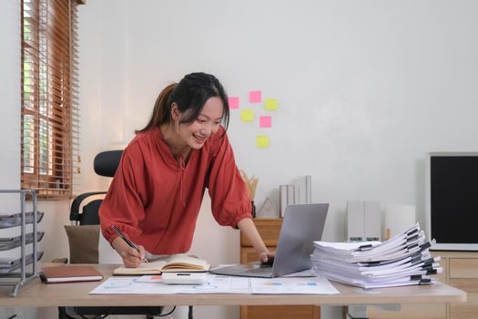 Young Asian businesswoman taking notes using a laptop at the modern office..