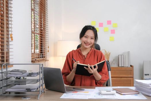 Young Asian businesswoman taking notes using a laptop at the modern office..