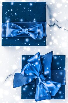 Branding, glamour and cold season concept - Winter holiday gift box with blue silk bow, snow glitter on marble background as Christmas and New Years presents for luxury beauty brand, flatlay design