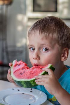Cute boy eating watermelon at home. Real emotions without posing. children