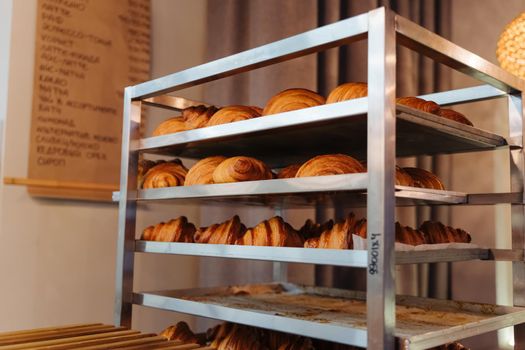 Production of delicious buns. Family bakery. Hot croissants on a metal tray. Fresh bakery. Rack with baked croissants.