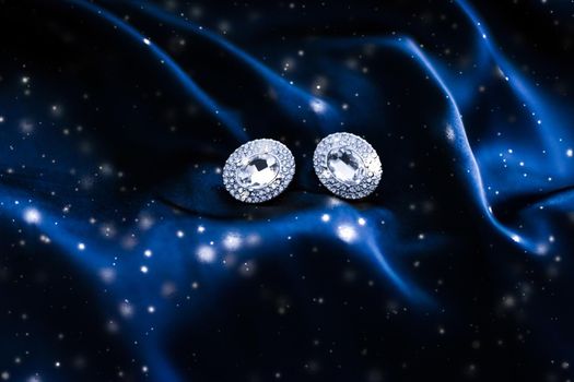 Jewellery brand, Christmas shopping and New Years gift concept - Luxury diamond earrings on dark blue silk with snow glitter, holiday winter magic jewelery present