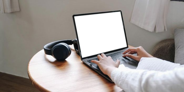 Girl typing on laptop with blank screen, headphones on wooden table, mock up.
