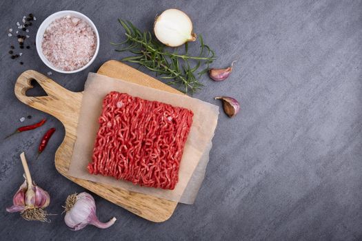 Minced meat lies on a cutting board surrounded by cooking ingredients. Top view with place for text. Selective focus.