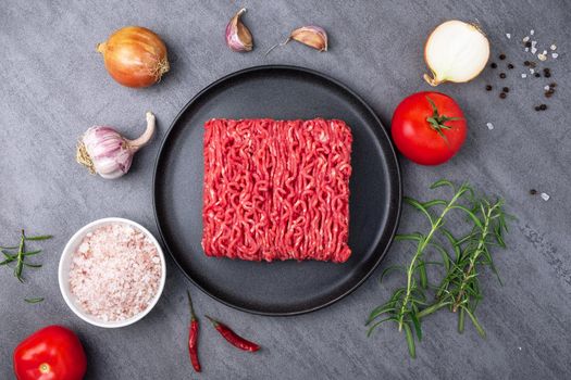 Minced meat lies on a black ceramic plate surrounded by cooking ingredients. View from above. Selective focus.