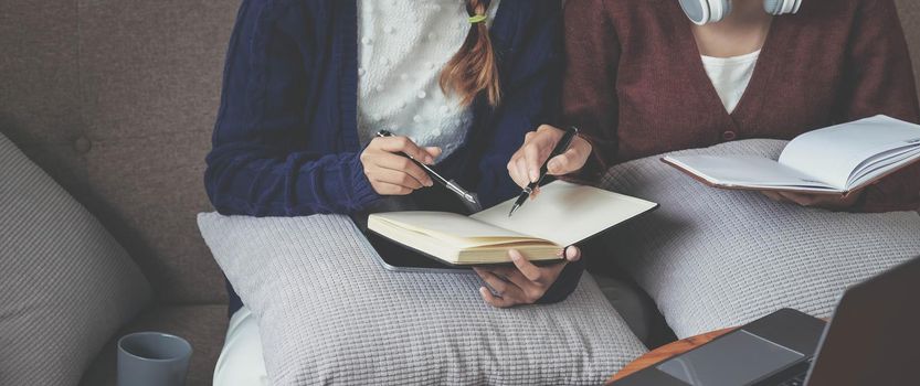 two young woman thinking with a book on sofa in living room at home.