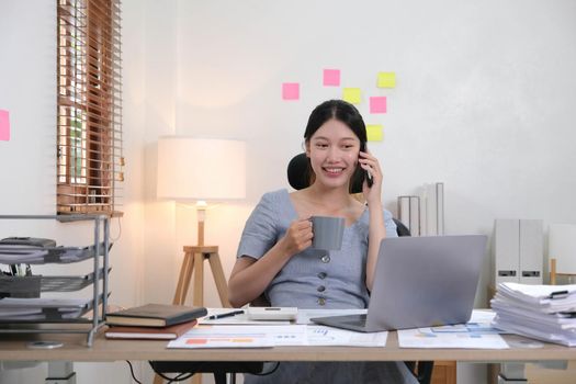 Business asian woman using smartphone for do math finance on wooden desk in office, tax, accounting, financial concept.