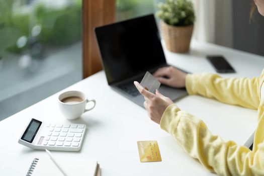 Close up of girl hold bank credit card and type on laptop, shopping online using computer, buying goods or ordering online, entering bank accounts and details in online banking offer.