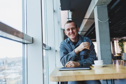 Handsome male manager sits at a table in a modern office with a closed laptop and rests, remote work