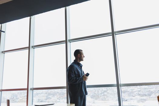 Young business man holding a phone. In an office or business center against the background of large windows of a skyscraper. Work and career, concept