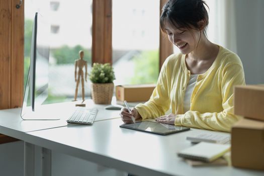 Young asian creative designer holding stylus pen drawing on screen of digital tablet while sitting at modern office