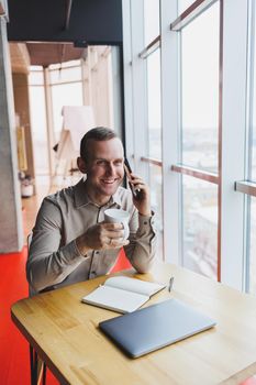 A young smart man is sitting in the office with a cup of coffee and is working on a project related to public cyber technology. Businessmen with laptop trying to meet deadlines in external marketing.
