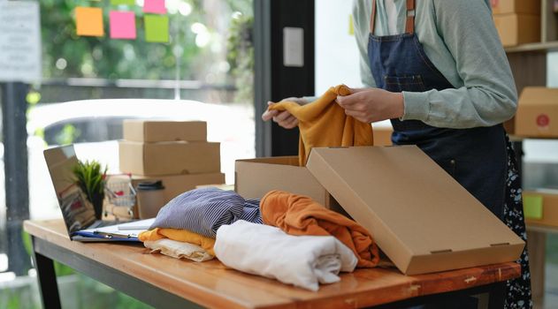 Young asian startup entrepreneur small business owner working at home, packaging clothes in box and delivery situation.