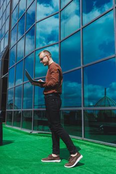 Cheerful businessman, formally dressed, pleased with received good news about contract details, sitting on office terrace with laptop, successful male entrepreneur