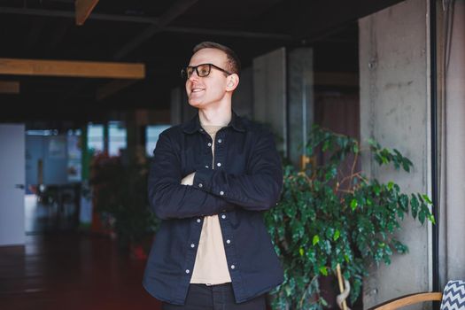 Half-length portrait of happy man in optical glasses holding modern mobile phone and smiling at camera, cheerful blogger with digital smartphone posing in coworking space