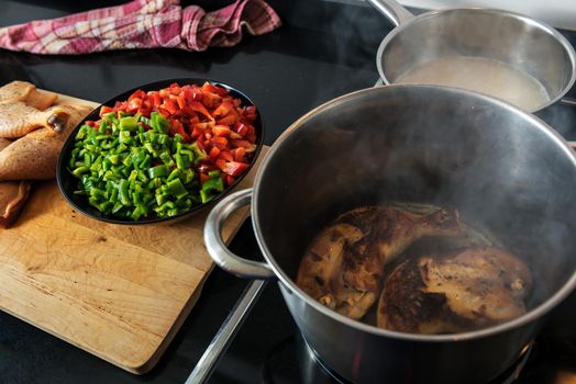 chicken fried in a pot, to cook it with the red and green pepper that are chopped on the plate on the wooden board, and the soup in the other pot