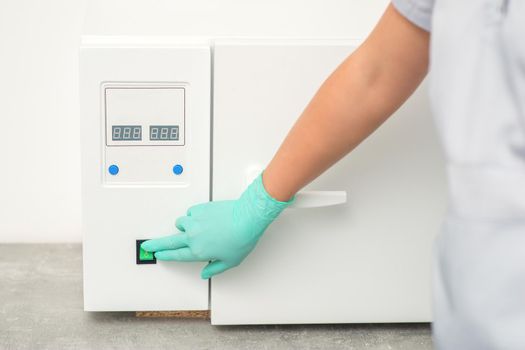 Beautician in protective gloves starts the machine for disinfection of tools before the medical procedure