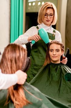 The hairdresser dries hair with a hairdryer of the beautiful young caucasian woman in the beauty salon