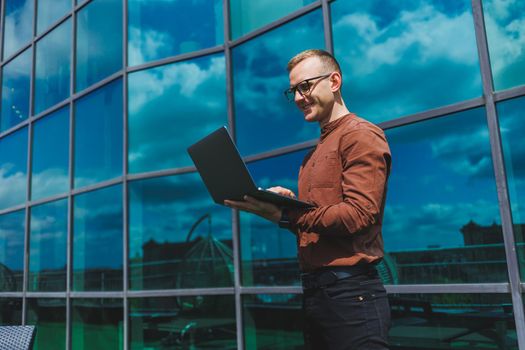 Cheerful businessman, formally dressed, pleased with received good news about contract details, sitting on office terrace with laptop, successful male entrepreneur