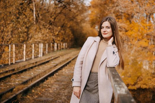 A beautiful long-haired woman walks through the autumn streets. Railway, autumn leaves, a woman in a light coat.