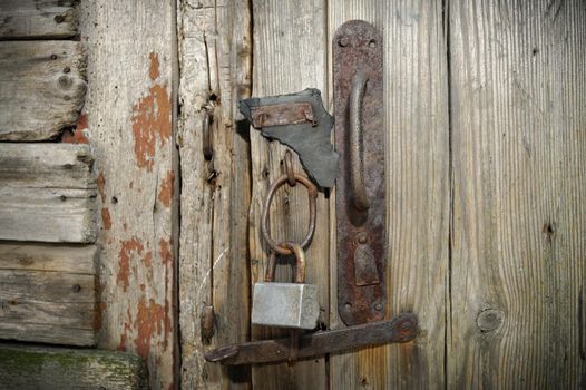 Old Wooden Door With A Rusty Steel Lock. Farm Gate From Planks With An Old Padlock. The Lock On The Door Of The Shed. Reliable Old Barn Rusty Padlock On A Wooden Door. Old Latch Of A Wooden Door Of A Cow Shed.