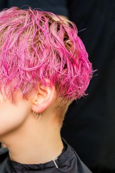 Beautiful young caucasian woman receiving new short pink hairstyle in hairdresser salon