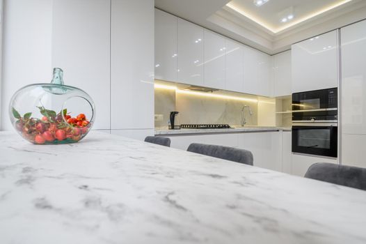 White kitchen interior, a vase with fruits at marble counter top at foreground