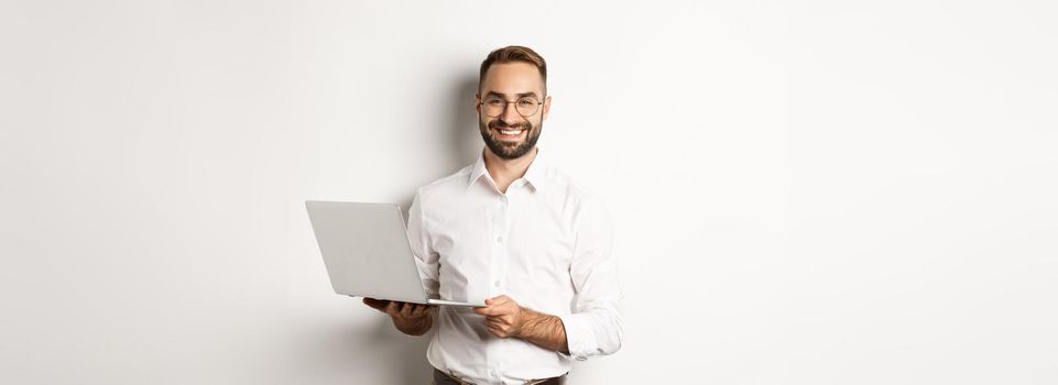 Business. Sucessful businessman working with laptop, using computer and smiling, standing over white background.