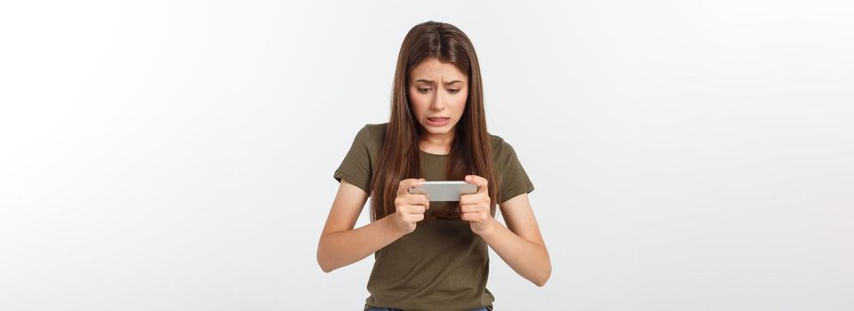 Happy attractive brunette girl joying win in video game on smartphone, isolated over grey background.