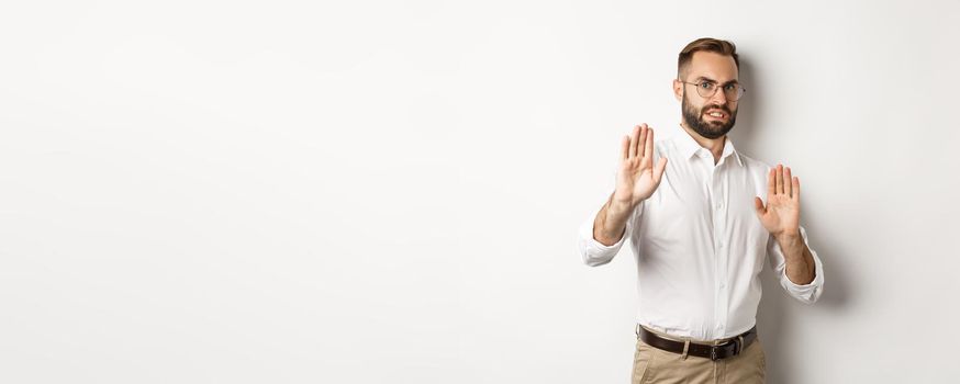 Displeased man rejecting something disturbing, showing stop sign and declining, cringe from aversion, standing over white background.