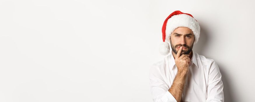 Party, winter holidays and celebration concept. Serious man thinking about christmas and new year, wearing santa hat, white background.