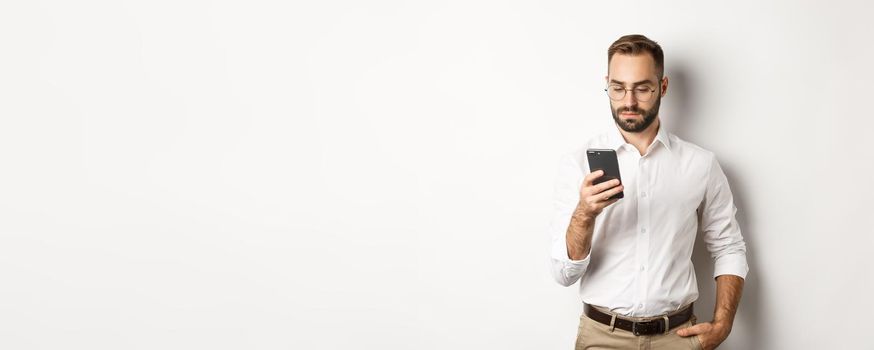 Businessman reading message on phone, standing over white background.