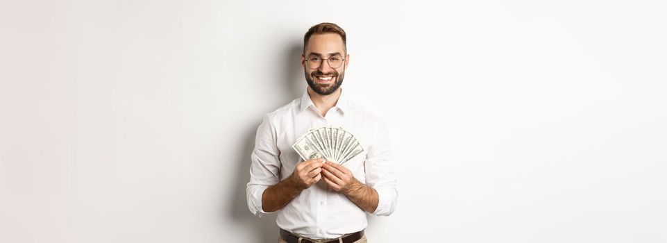 Smiling handsome man holding money, showing dollars, standing over white background. Copy space