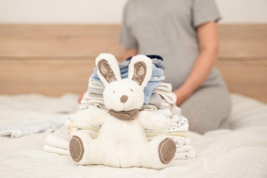 Pile of baby clothes, rabbit and pregnant woman