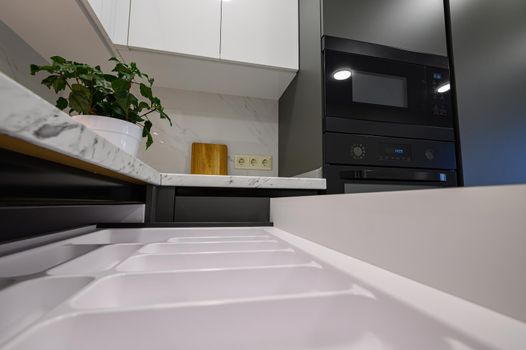 Closeup to marble worktop of modern dark grey and white kitchen, cooking pan at gas cooker, cabinet drawers retracted