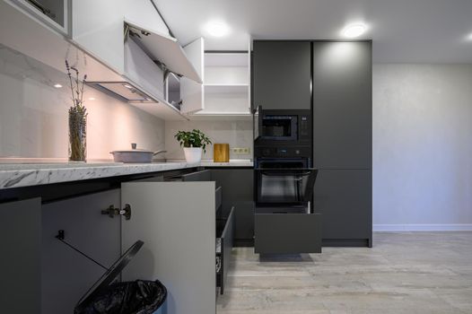 Showcase interior of modern simple dark grey and white kitchen, drawers retracted, doors open