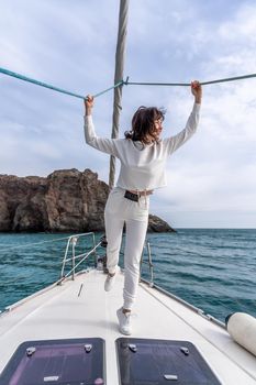 Woman standing on the nose of the yacht at a sunny summer day, breeze developing hair, beautiful sea on background.