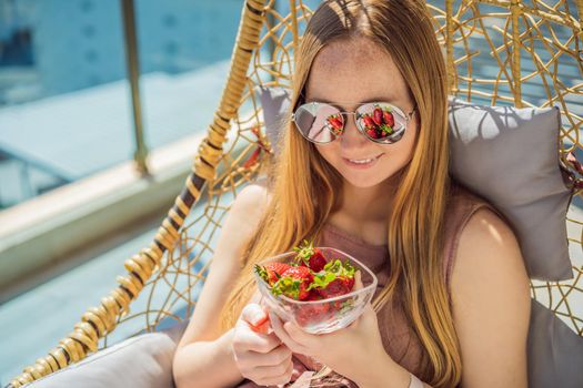 Portrait of gorgeous woman wearing beautiful dress sitting in a patio and eating strawberry.