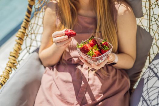 Portrait of gorgeous woman wearing beautiful dress sitting in a patio and eating strawberry.