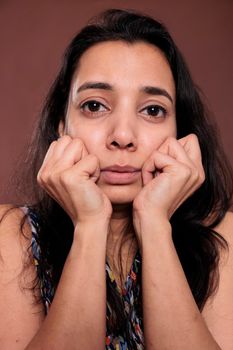 Indian woman holding clenched fists on cheeks closeup portrait, cute pose. Calm lady touching face with hands close view, person with neutral facial expression looking at camera