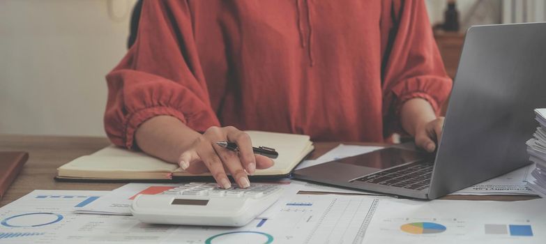 Business woman using calculator and laptop for do math finance on wooden desk in office and business working background, tax, accounting, statistics and analytic research concept.