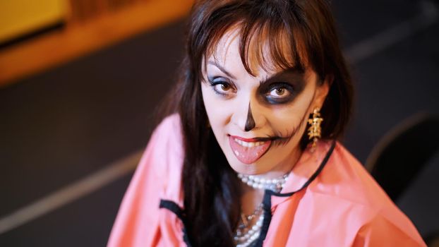 Halloween party, make-up artist draws a terrible makeup on the face of a brunette woman for a Halloween party. in the background, the scenery in the style of Halloween is seen. High quality photo