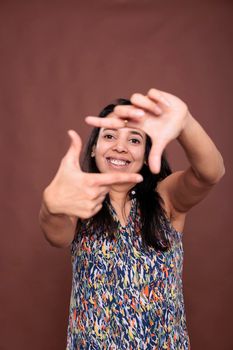 Smiling indian woman making photo frame gesture with fingers, looking at camera. Cheerful photographer posing portrait, front view studio medium shot, photography, imaginable photoshoot