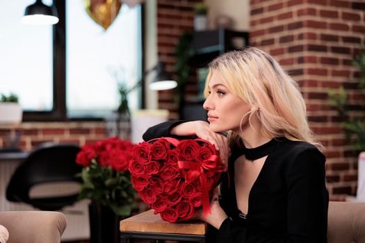 Beautiful thoughtful woman holding roses, side view, valentines day gift. Attractive blonde girl with flower bouquet in heart shaped box posing, love holiday romantic celebration.