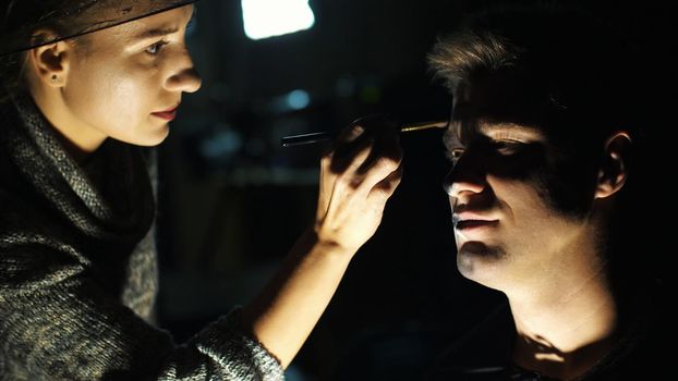 Halloween party, close-up, make-up artist draws a terrible makeup on the face of a man for a Halloween party. High quality photo