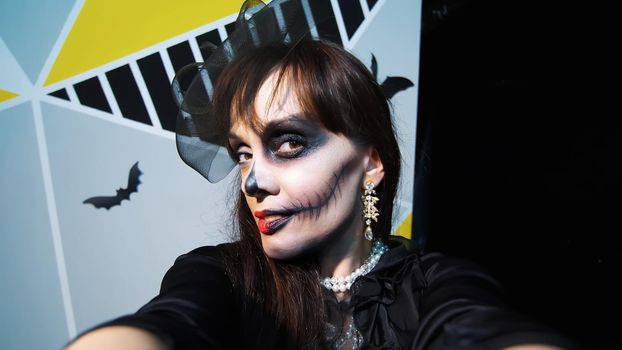 Halloween party, night, frightening portrait of a woman with a terrible makeup in a black witch suit, croaks in front of the camera. High quality photo