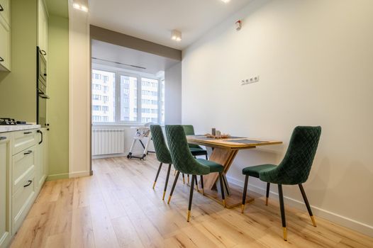 Modern trendy light green luxurious kitchen with dining table and dark green chairs