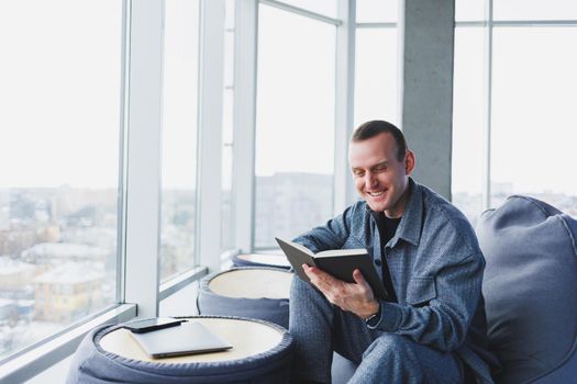 A male businessman in a casual suit resting in a comfortable pouf while working, an attractive freelancer in a suit works remotely and checks notes in a notebook