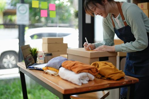 Young asian girl is freelancer Start up small business owner writing address on cardboard box at workplace,Shipping shopping online small business entrepreneur SME or freelance.