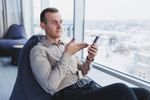 A businessman communicates with his clients by phone while sitting in a modern office workspace. Focused businessman sits alone in a modern workspace.